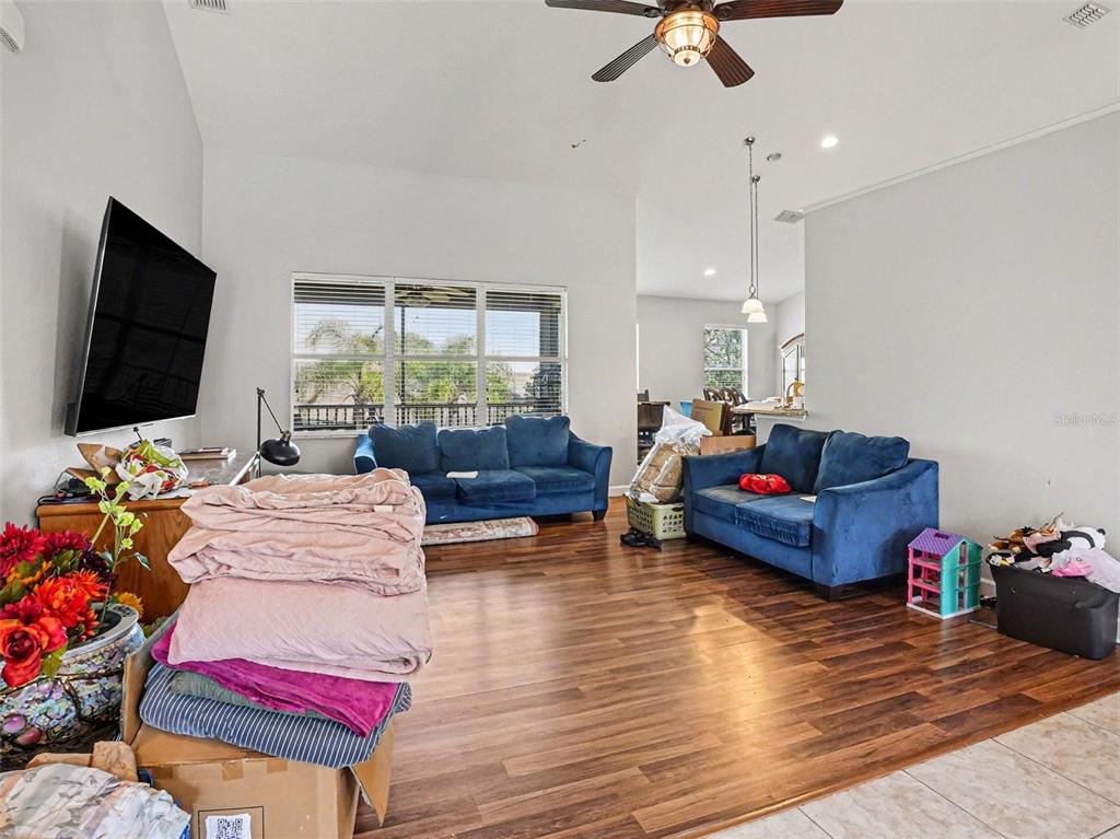 A living room features vaulted ceilings, wood-look flooring, a wall-mounted television, and blue furniture — 1042 HARMONY LANE, CLERMONT, FL