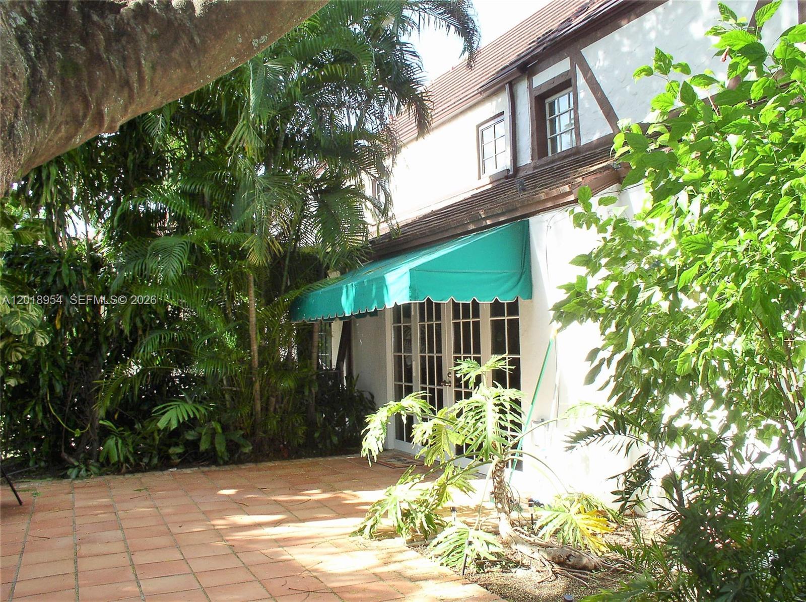 A patio with terracotta tiles sits beside a white house with a green awning — 404 Viscaya Ave # 404, Coral Gables FL 33134, CORAL GABLES, FL