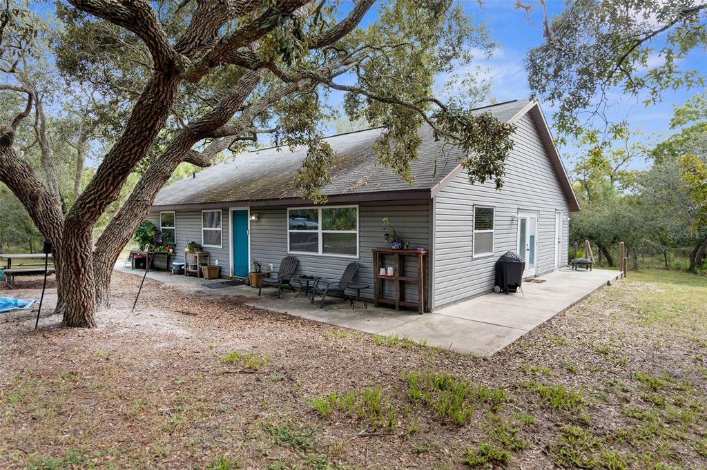 A gray, single-story house with a concrete patio sits under large oak trees — 15236 MOTTLED OWL ROAD, BROOKSVILLE, FL
