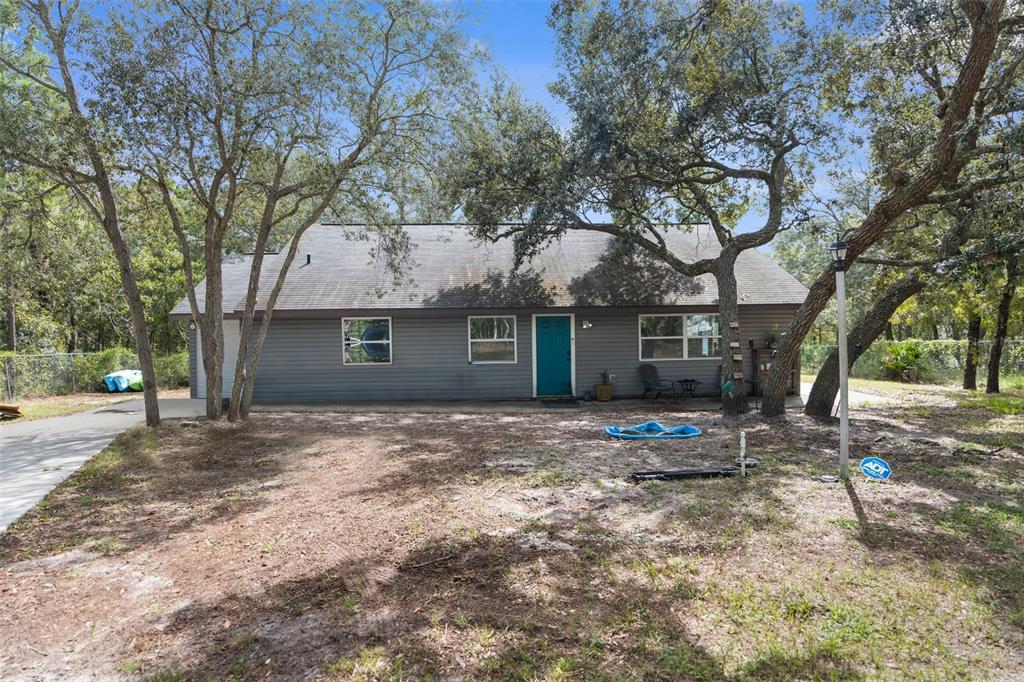 A gray, single-story house with a teal front door sits on a wooded, sandy lot — 15236 MOTTLED OWL ROAD, BROOKSVILLE, FL