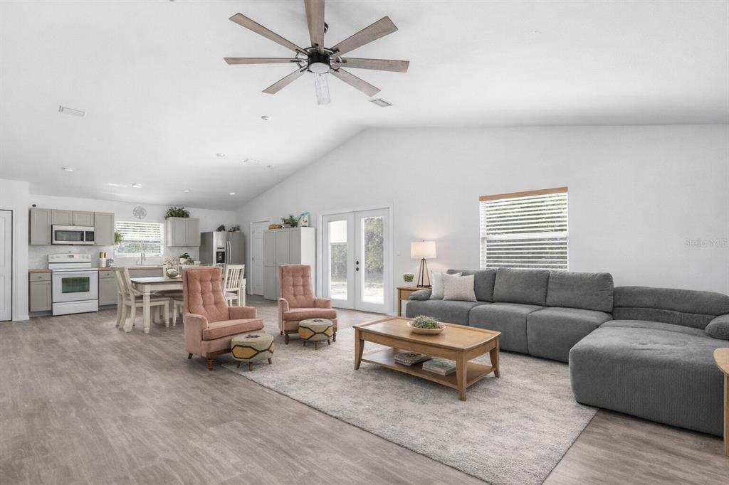 An open-concept living room and kitchen featuring gray cabinetry, a sectional sofa, and wood-look flooring — 15236 MOTTLED OWL ROAD, BROOKSVILLE, FL