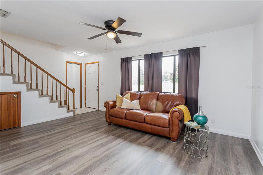 A living room features a brown leather sofa, wood-look flooring, and a staircase with railings — 2134 NE 45TH AVENUE, OCALA, FL