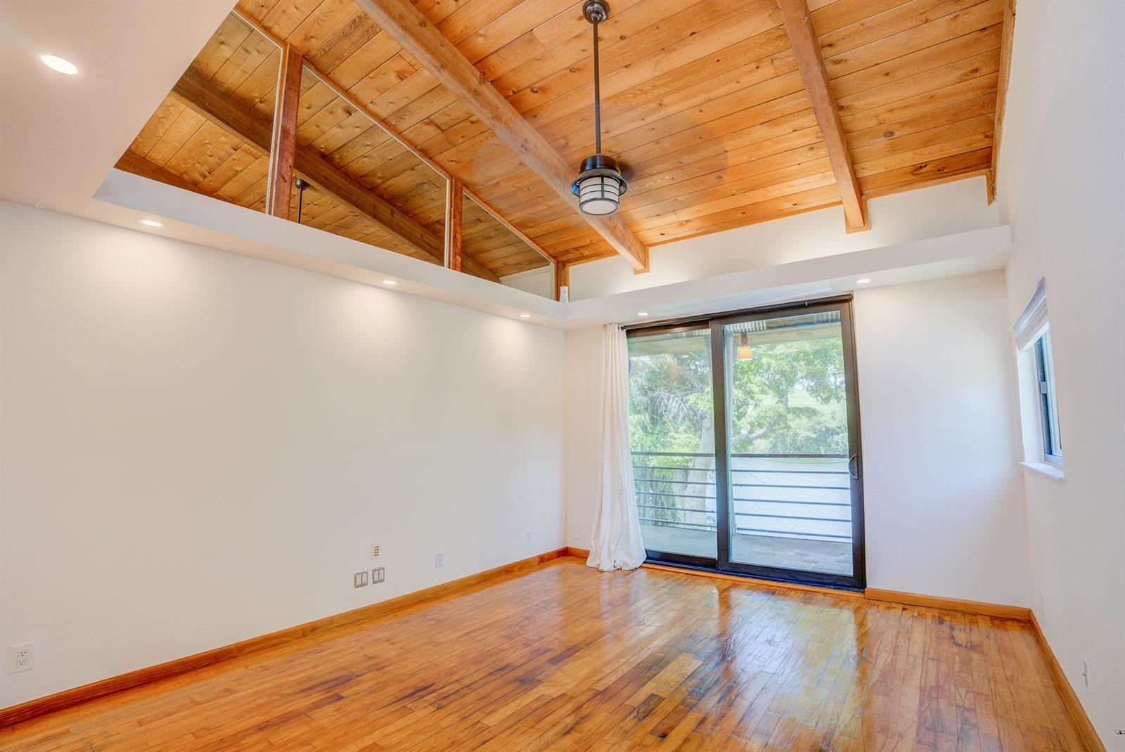 An empty room features hardwood floors, a vaulted wood-plank ceiling with beams, and sliding glass doors — 4491 Crystal Lake Drive # 201a, Pompano Beach FL 33064, POMPANO BEACH, FL