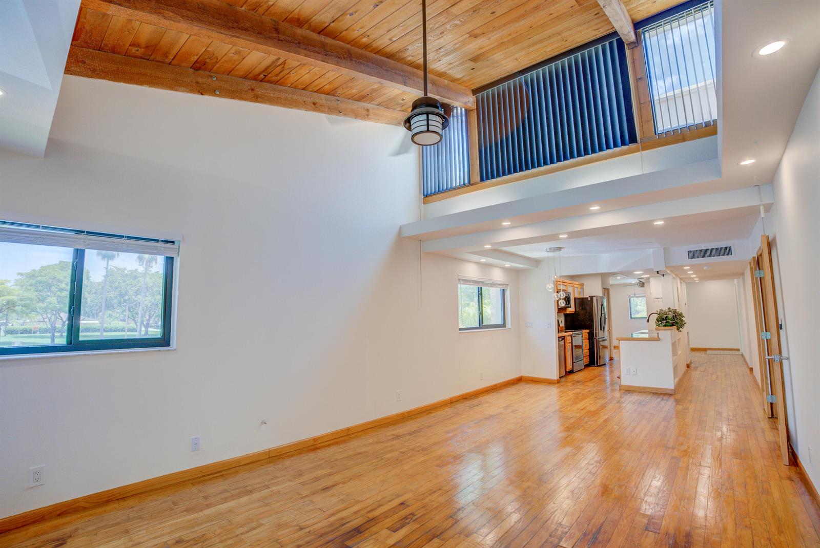 A living room with hardwood floors, vaulted wood-beam ceilings, and an open kitchen beyond — 4491 Crystal Lake Drive # 201a, Pompano Beach FL 33064, POMPANO BEACH, FL