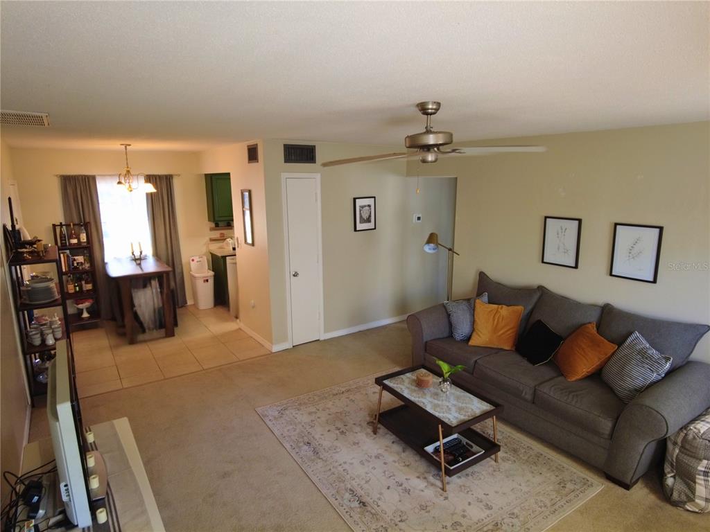 A living room with carpeted floors, a gray sofa, and an adjacent dining area — 6930A PLACE DE LA PAIX UNIT 2B, SOUTH PASADENA, FL