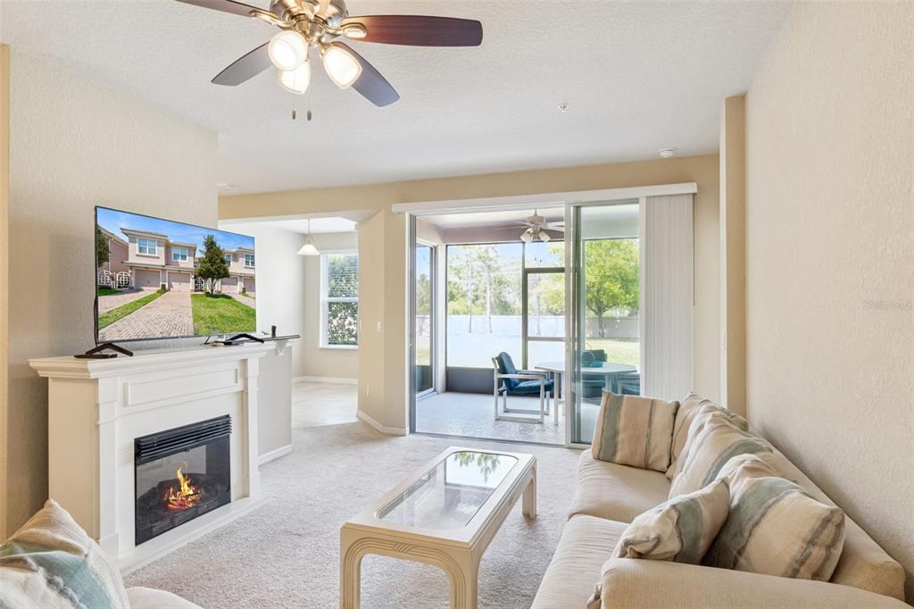 A living room features a fireplace, a television, a ceiling fan, and a screened-in patio — 8349 BELLA TIERRA COURT, DAVENPORT, FL