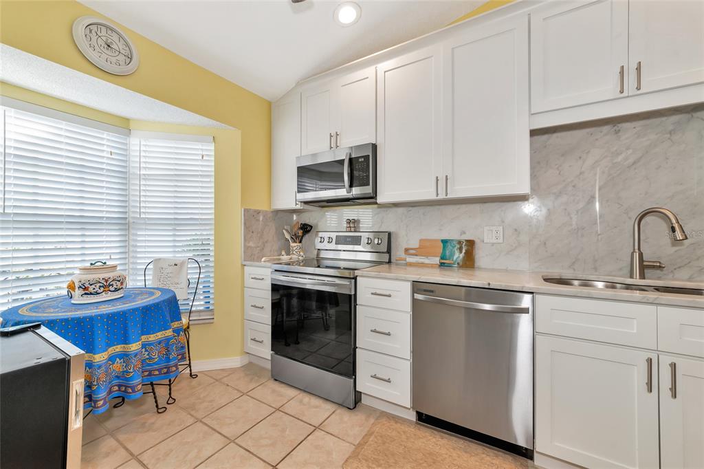 A kitchen features white cabinets, stainless steel appliances, a marble backsplash, and a breakfast nook — 504 WOODSTORK CIRCLE, BRADENTON, FL