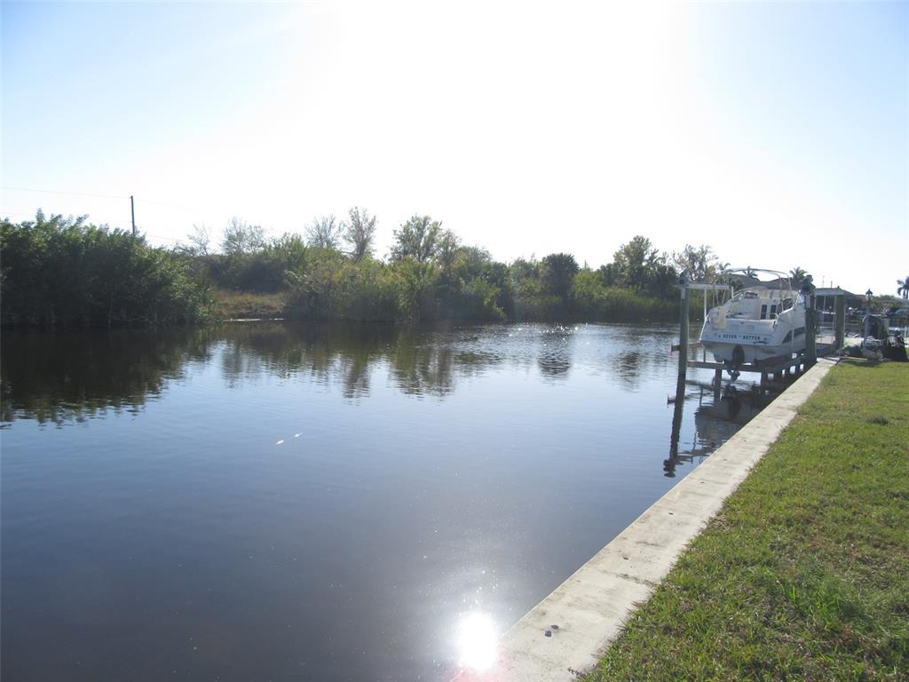 A boat sits on a lift along a concrete seawall bordering a calm canal — 9572 SINGER CIRCLE, PORT CHARLOTTE, FL