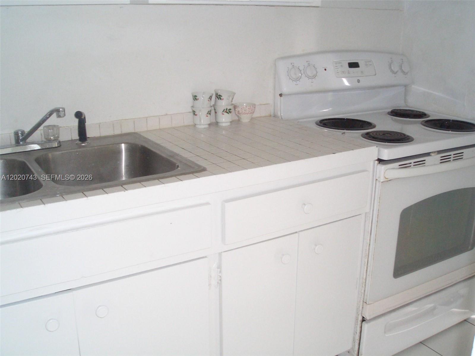 A kitchen features a stainless steel sink, tiled countertop, and a white electric stove — 9760 SW 184th St # 16D, Cutler Bay FL 33157, CUTLER BAY, FL