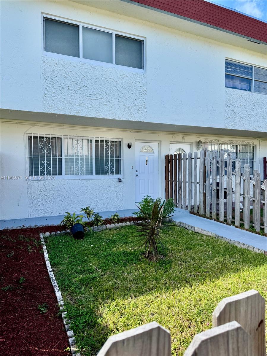 A two-story white stucco townhouse features a small front lawn and a wooden fence — 1481 NE 150th St # 102, Miami FL 33161, MIAMI, FL