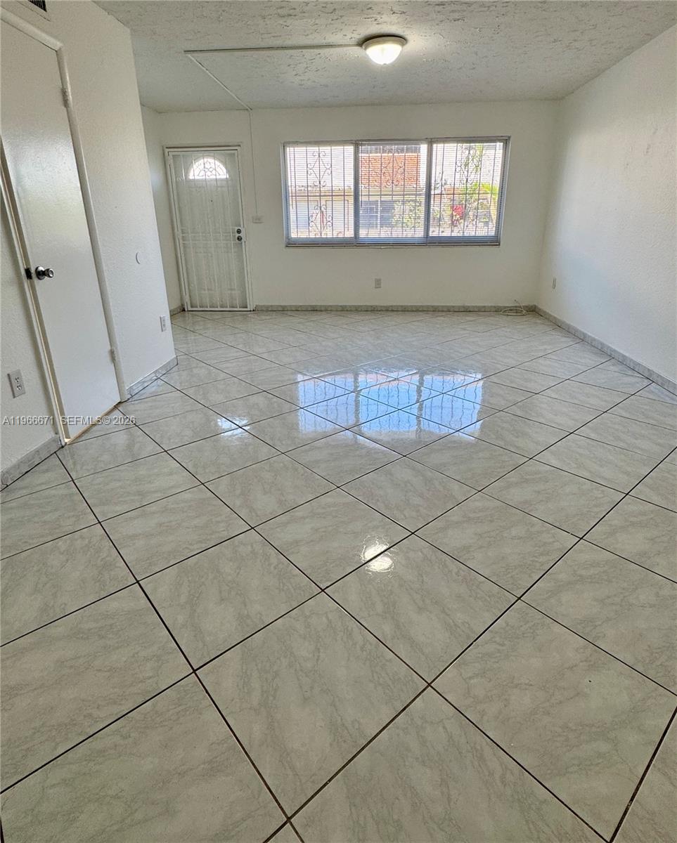 An empty room features white walls, large square floor tiles, and a window with security bars — 1481 NE 150th St # 102, Miami FL 33161, MIAMI, FL
