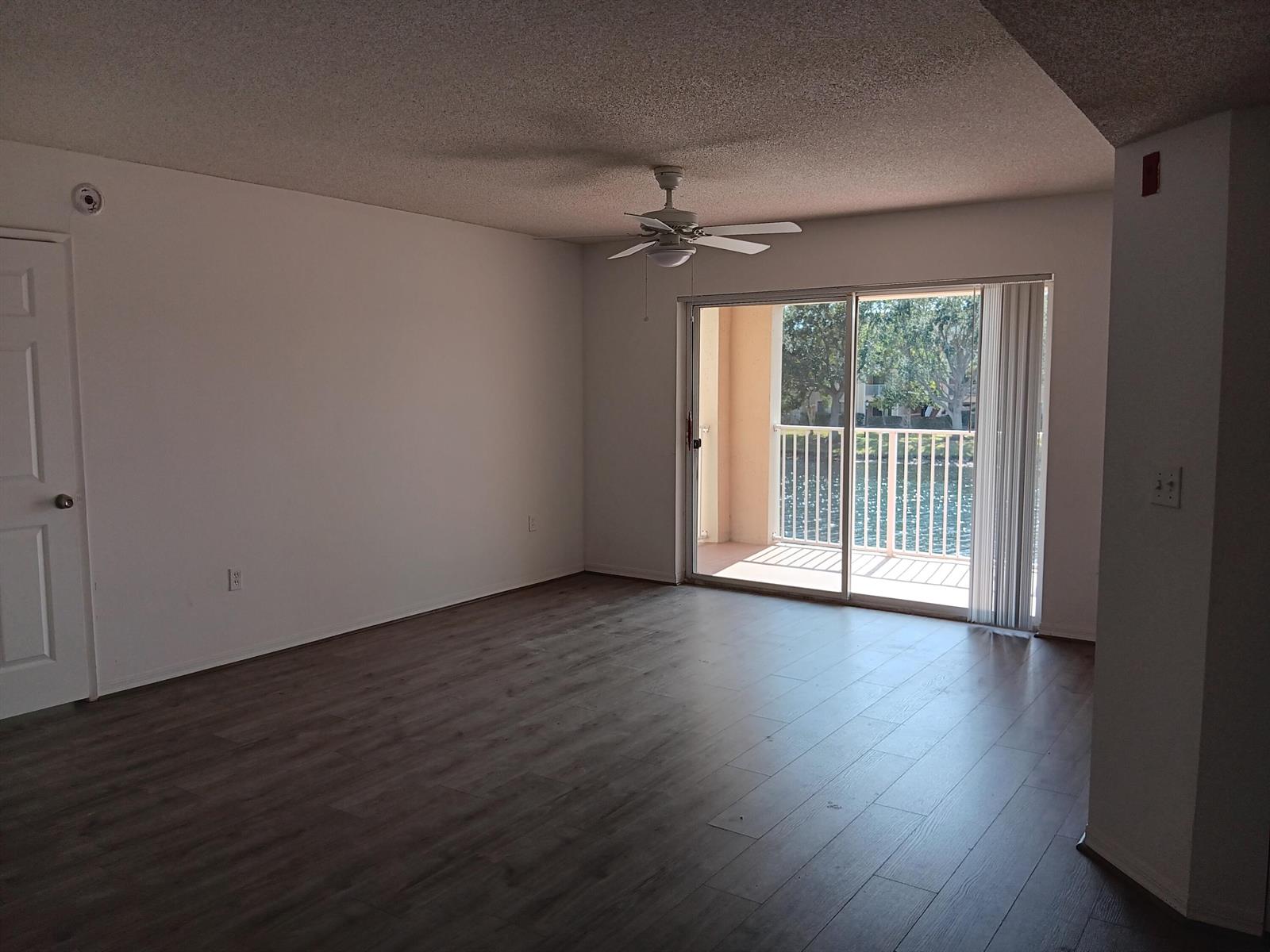 An empty living room with wood-look flooring, a ceiling fan, and a sliding glass door — 1640 N 42nd Circle # 204, Vero Beach FL 32967, VERO BEACH, FL