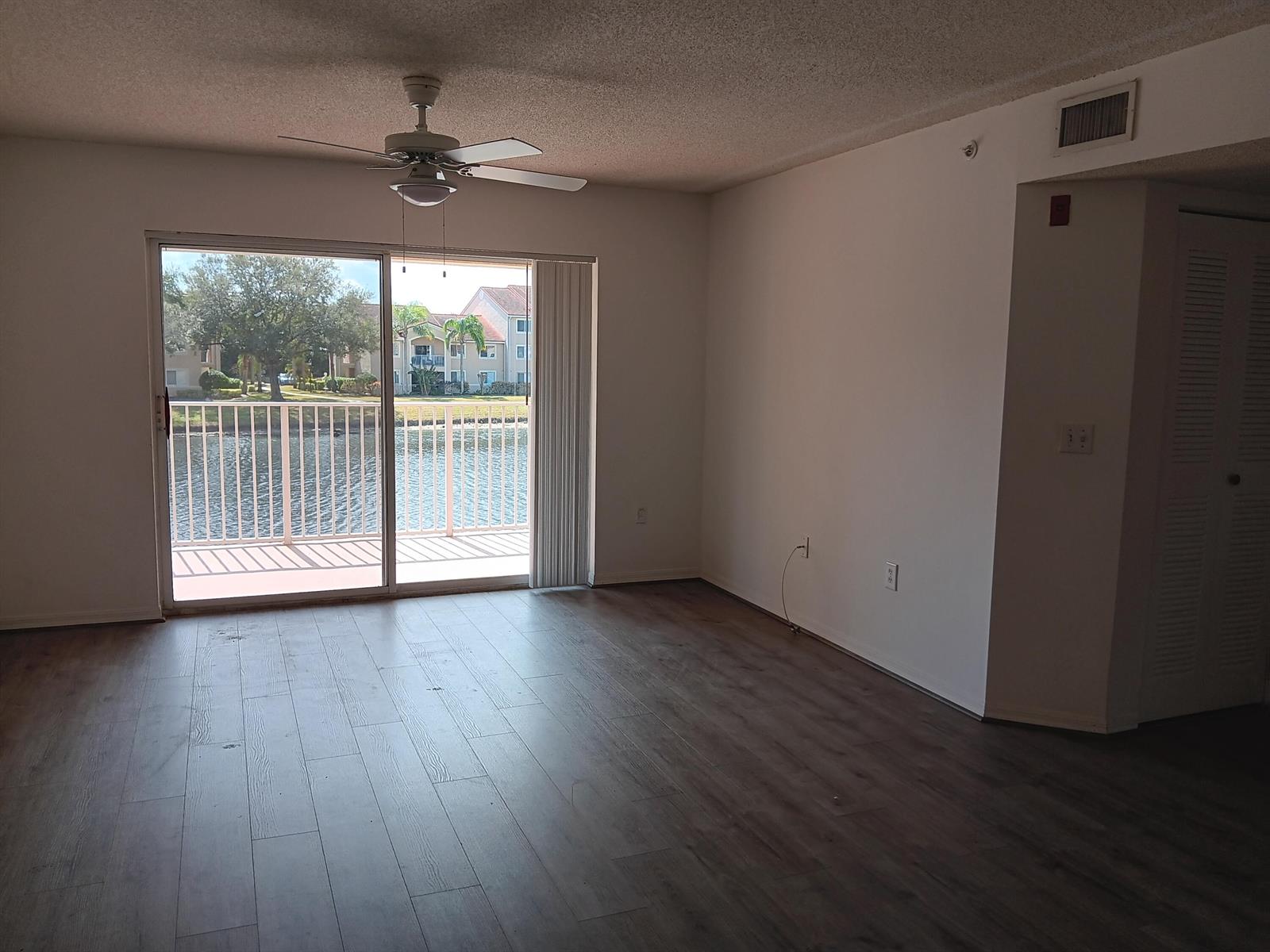 An empty living room with wood-look flooring, a ceiling fan, and sliding doors to a balcony — 1640 N 42nd Circle # 204, Vero Beach FL 32967, VERO BEACH, FL