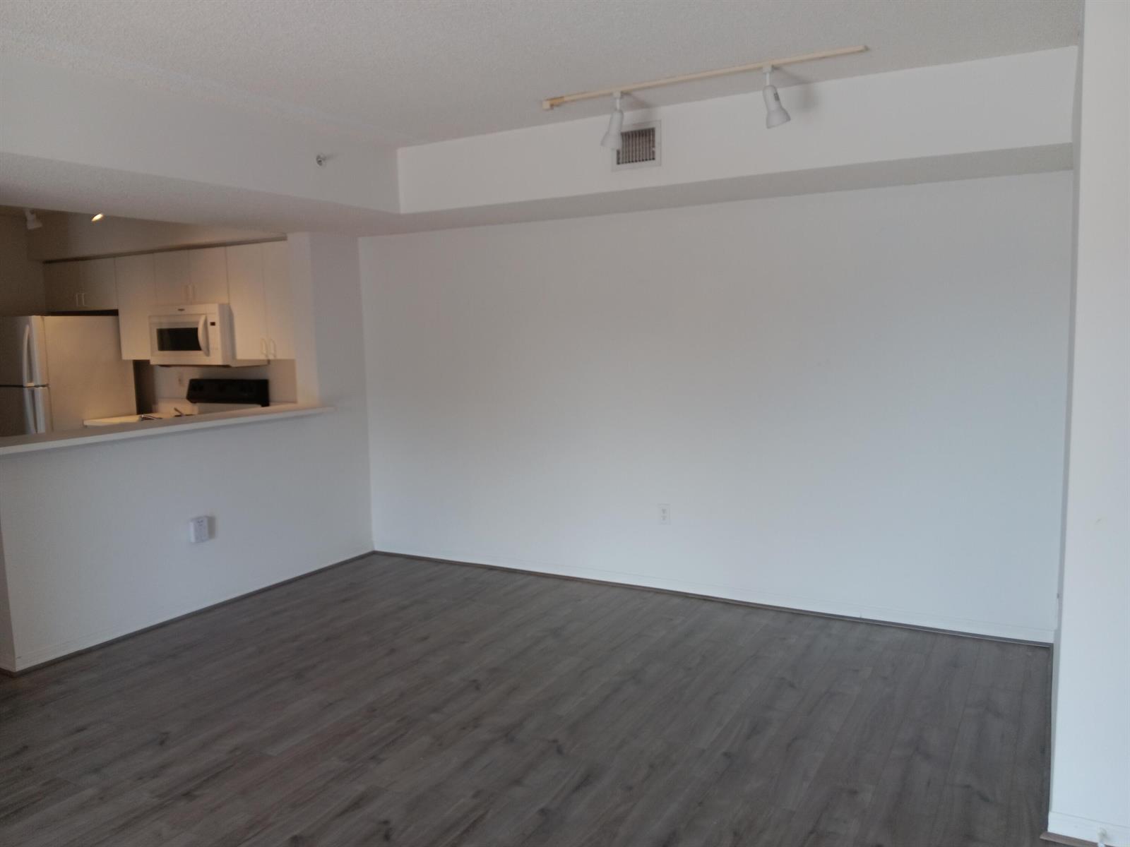 An empty living room with gray wood-look flooring, white walls, and a track lighting fixture — 1640 N 42nd Circle # 204, Vero Beach FL 32967, VERO BEACH, FL
