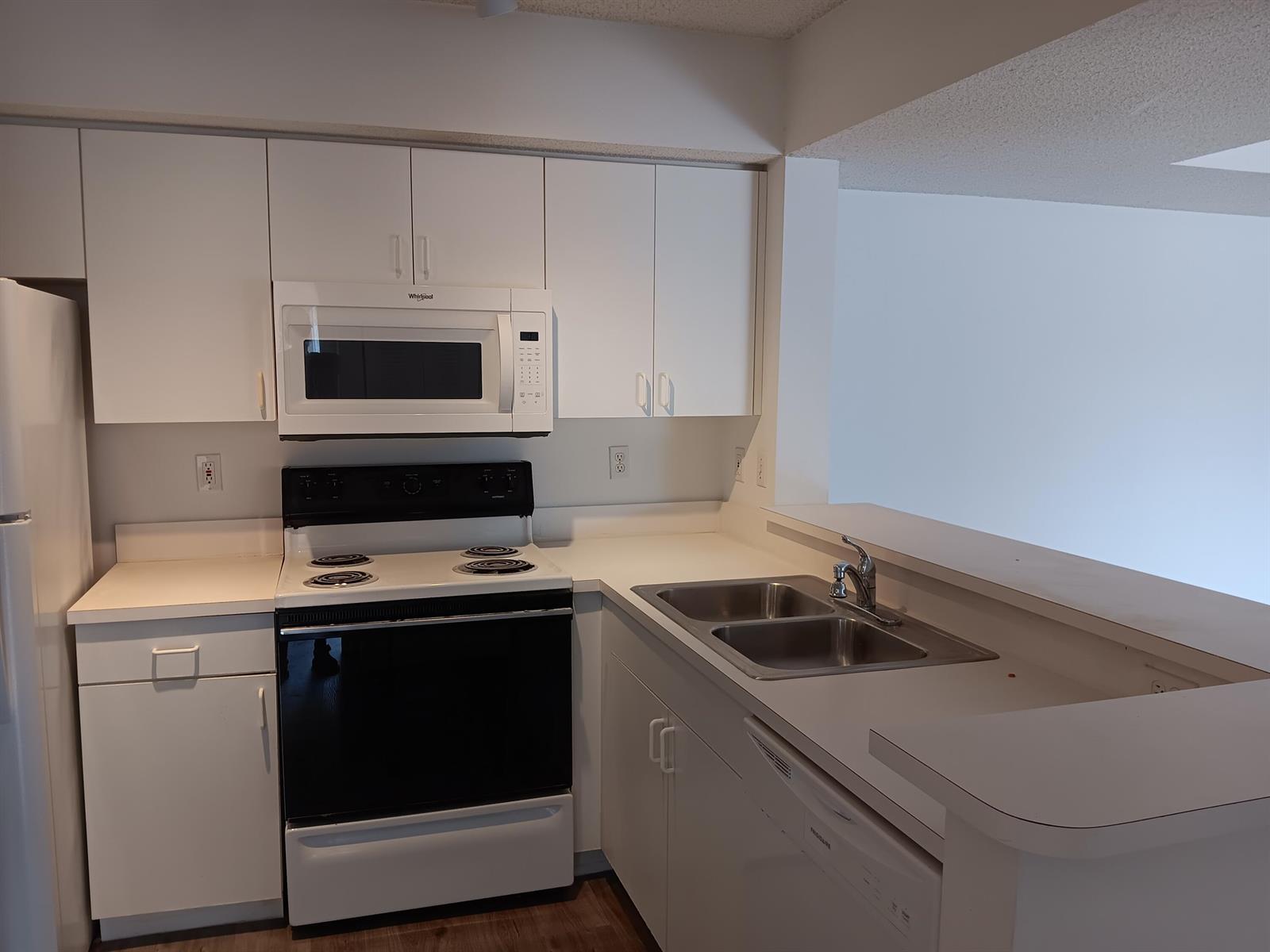 A kitchen features white cabinets, a black stove, a microwave, and a double sink — 1640 N 42nd Circle # 204, Vero Beach FL 32967, VERO BEACH, FL