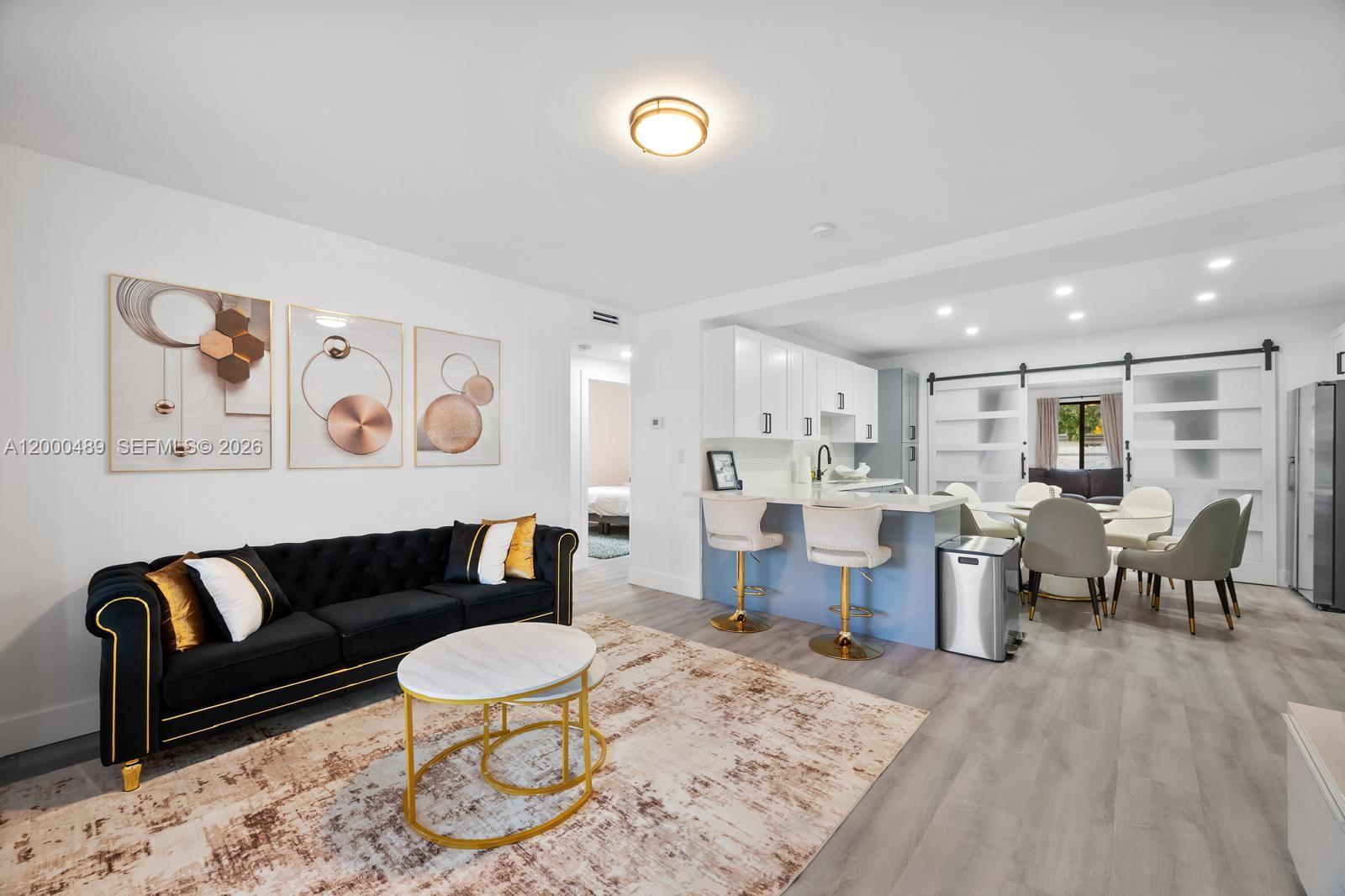 A modern living room and kitchen area features a black sofa, island seating, and dining table — 11730 NW 3rd Ave, Miami FL 33168, MIAMI, FL