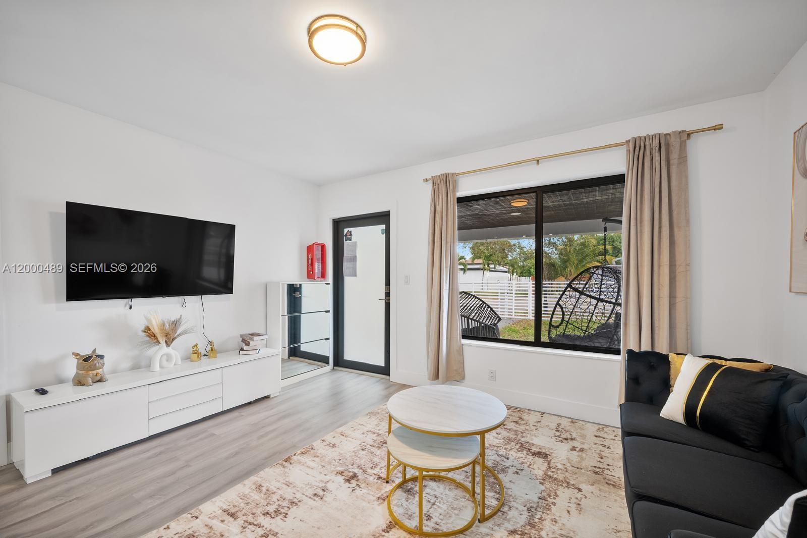 A living room features a wall-mounted television, white media console, and a large window — 11730 NW 3rd Ave, Miami FL 33168, MIAMI, FL