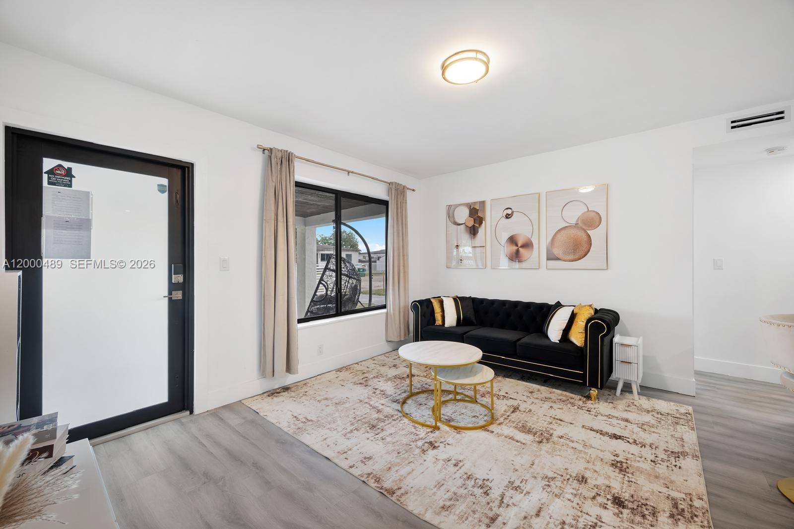 A living room features a black tufted sofa, a round coffee table, and light flooring — 11730 NW 3rd Ave, Miami FL 33168, MIAMI, FL