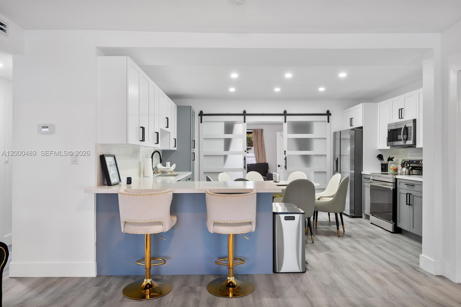 A modern kitchen features white cabinetry, a blue island with gold stools, and sliding barn doors — 11730 NW 3rd Ave, Miami FL 33168, MIAMI, FL