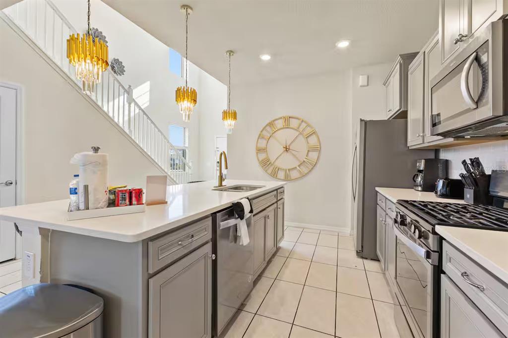 A kitchen with a central island, grey cabinetry, stainless steel appliances, and a large wall clock — 5405 MISTY OAK CIRCLE, DAVENPORT, FL