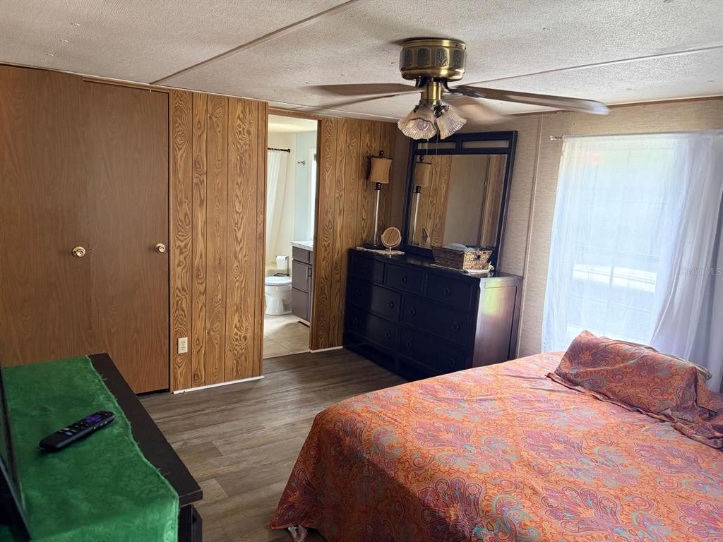 A bedroom features wood-paneled walls, a dark dresser with a mirror, and a patterned bedspread — 13322 SW 95TH STREET, DUNNELLON, FL