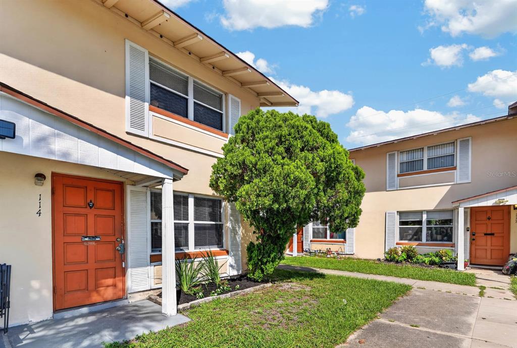 The exterior of a two-story apartment building features orange doors and a central green tree — 1600 S PALMETTO AVENUE UNIT 114, SOUTH DAYTONA, FL