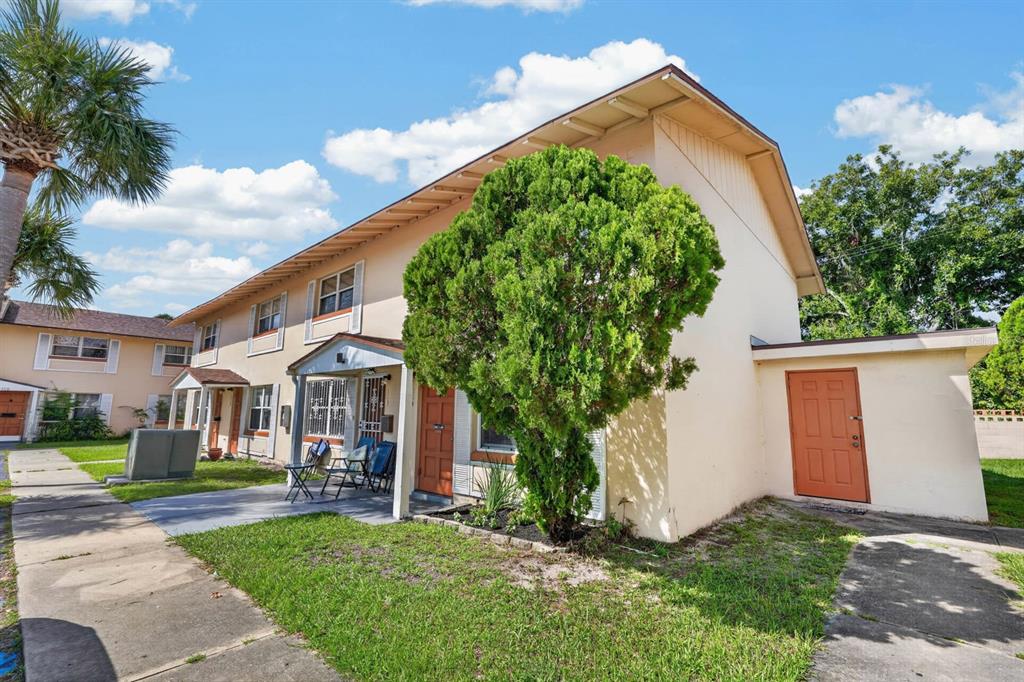 A two-story apartment building exterior with a tan facade, a large tree, and orange doors — 1600 S PALMETTO AVENUE UNIT 114, SOUTH DAYTONA, FL
