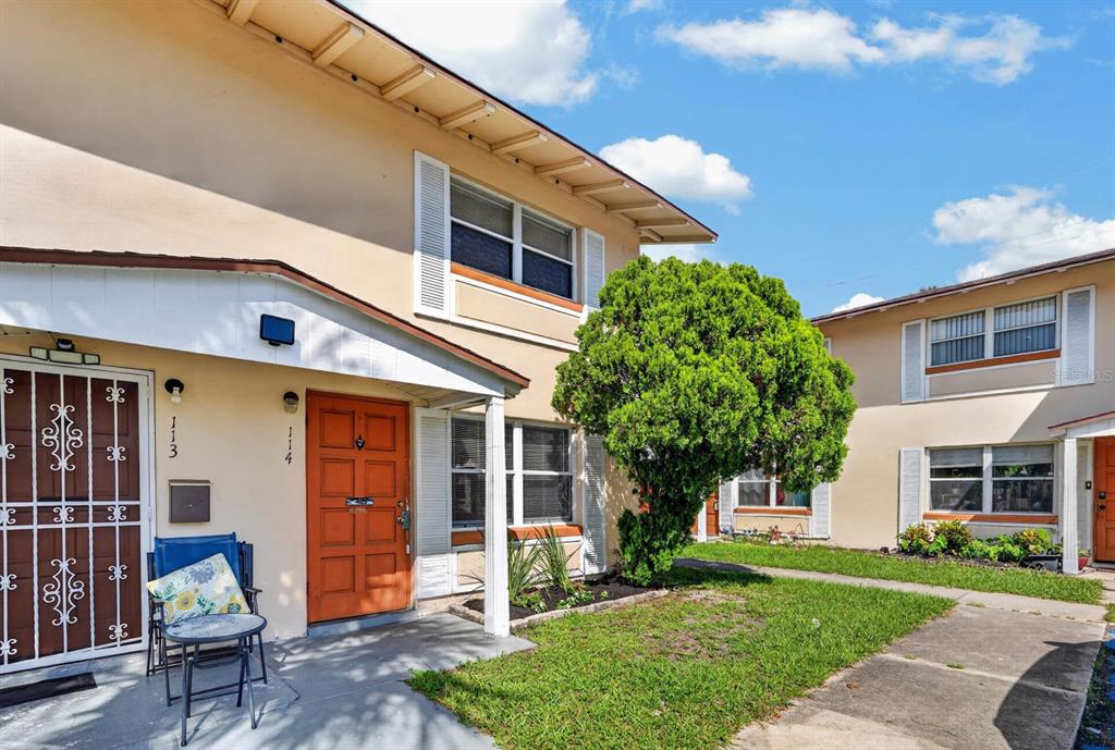 A two-story apartment building exterior features a tan facade, an orange door, and a small patio — 1600 S PALMETTO AVENUE UNIT 114, SOUTH DAYTONA, FL