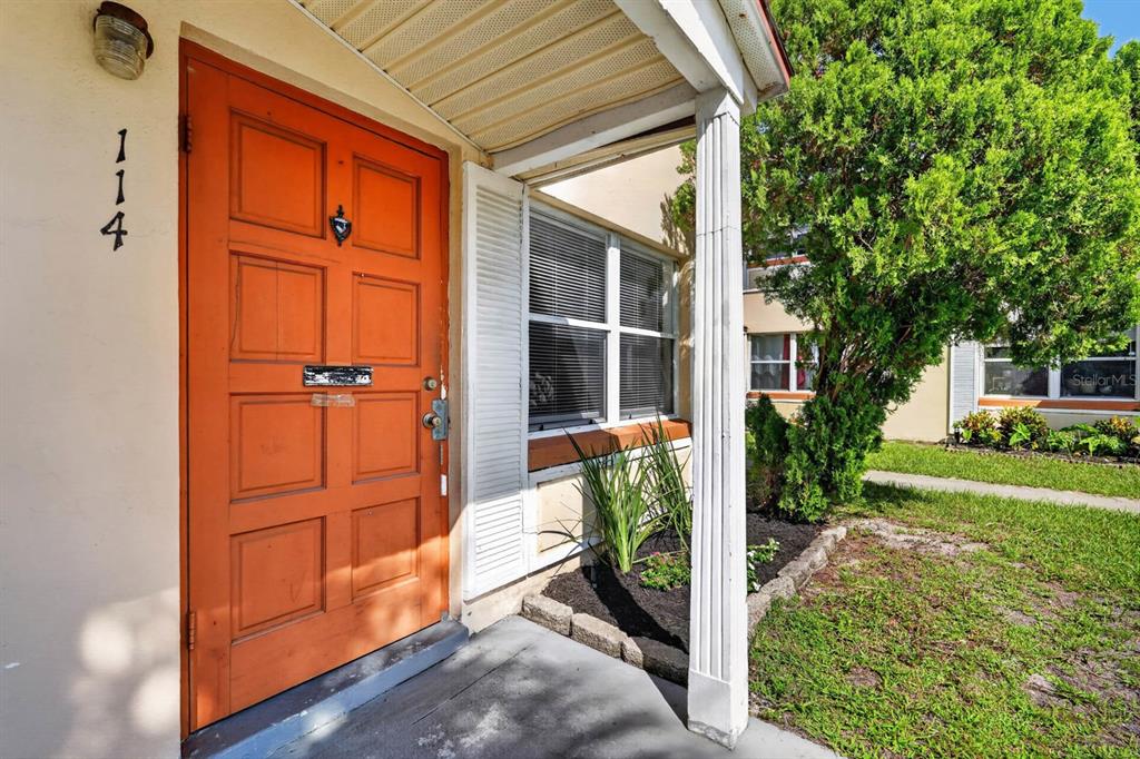 An orange front door with a house number 114 sits under a small covered porch — 1600 S PALMETTO AVENUE UNIT 114, SOUTH DAYTONA, FL