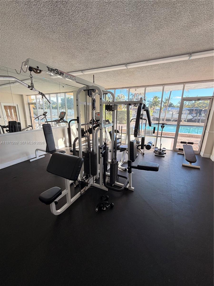 A home gym features a multi-station weight machine, black rubber flooring, and floor-to-ceiling windows — 2350 NE 135th St # 503, North Miami FL 33181, NORTH MIAMI, FL