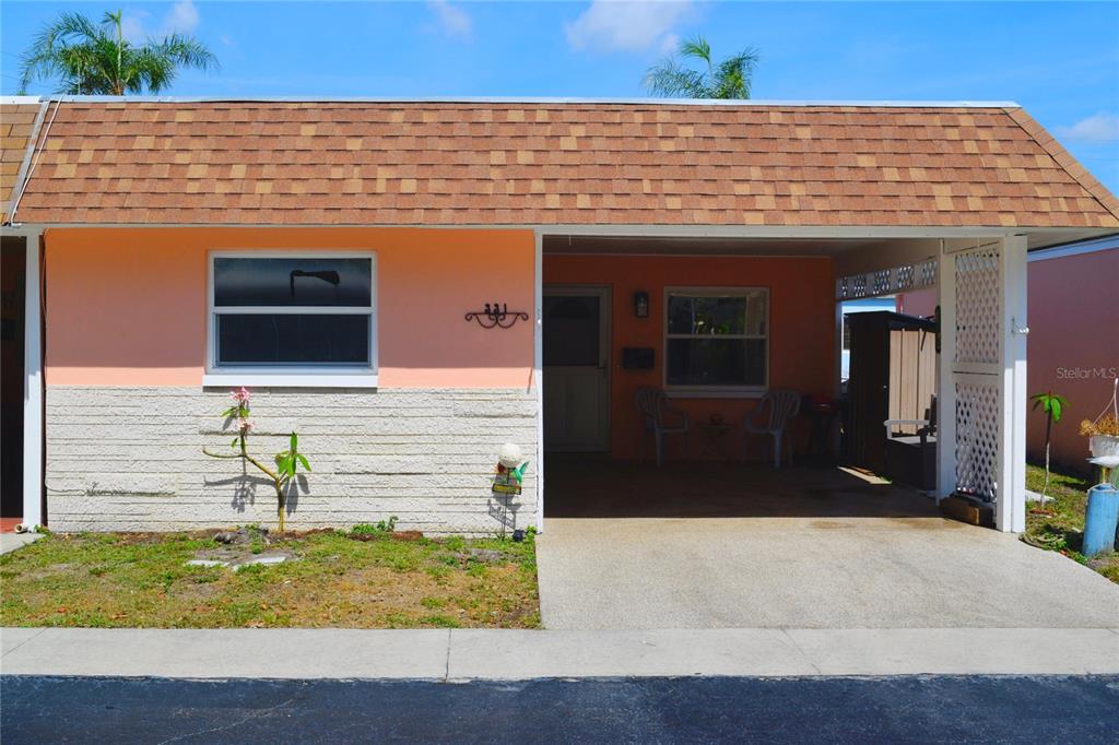 A single-story peach-colored house features a brown shingled roof, a carport, and stone siding — 331 SKY LOCH DRIVE W, DUNEDIN, FL