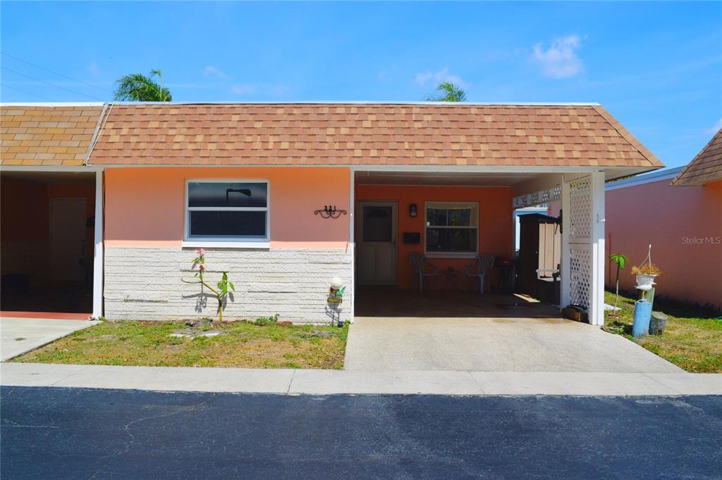 A single-story peach-colored house with a carport, white brick facade, and brown shingled roof — 331 SKY LOCH DRIVE W, DUNEDIN, FL