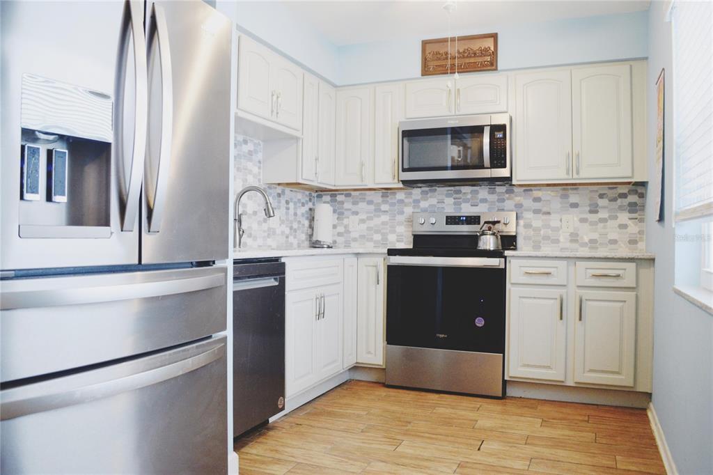 A kitchen with white cabinets, stainless steel appliances, and a mosaic tile backsplash — 331 SKY LOCH DRIVE W, DUNEDIN, FL