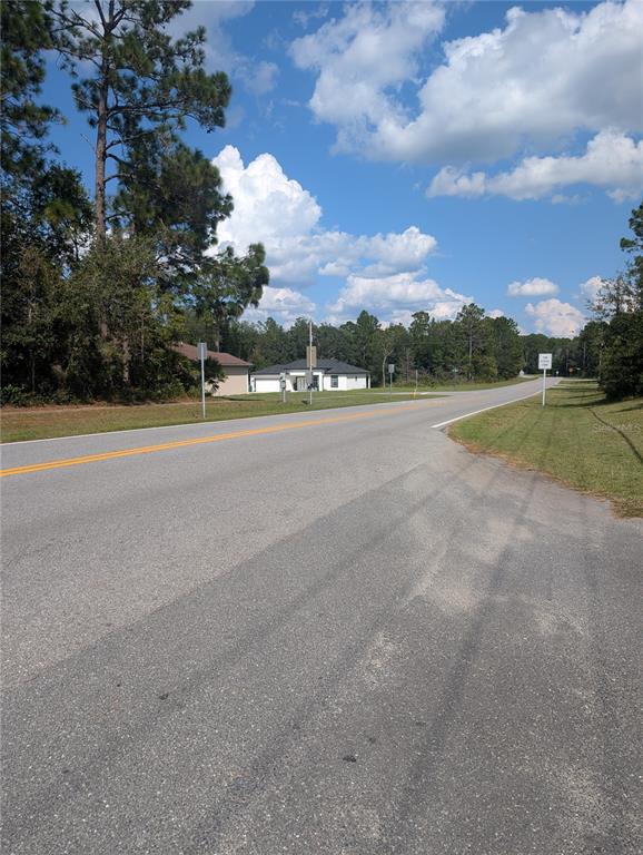 A paved road stretches toward a modern house surrounded by trees under a blue sky — 3515 W CENTURY BOULEVARD, CITRUS SPRINGS, FL
