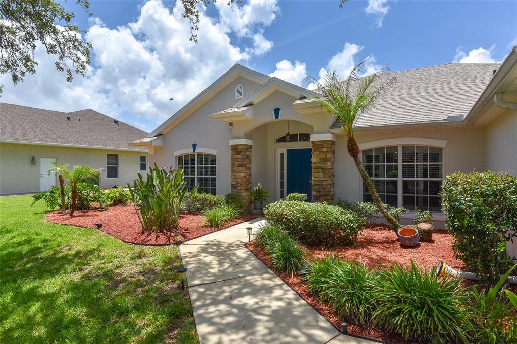 A single-story house with a blue front door, stone columns, and red mulch landscaping — 736 ALDENWOOD TRAIL, NEW SMYRNA BEACH, FL