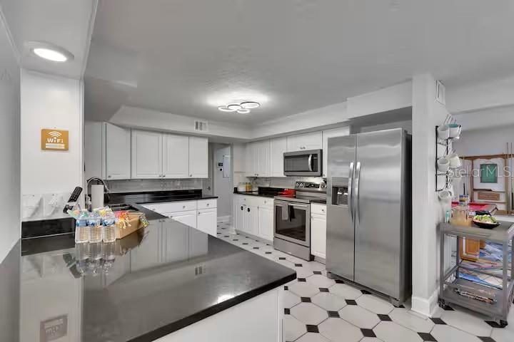 A kitchen features white cabinets, black countertops, stainless steel appliances, and black-and-white tiled flooring — 10712 DALTON AVENUE, TAMPA, FL