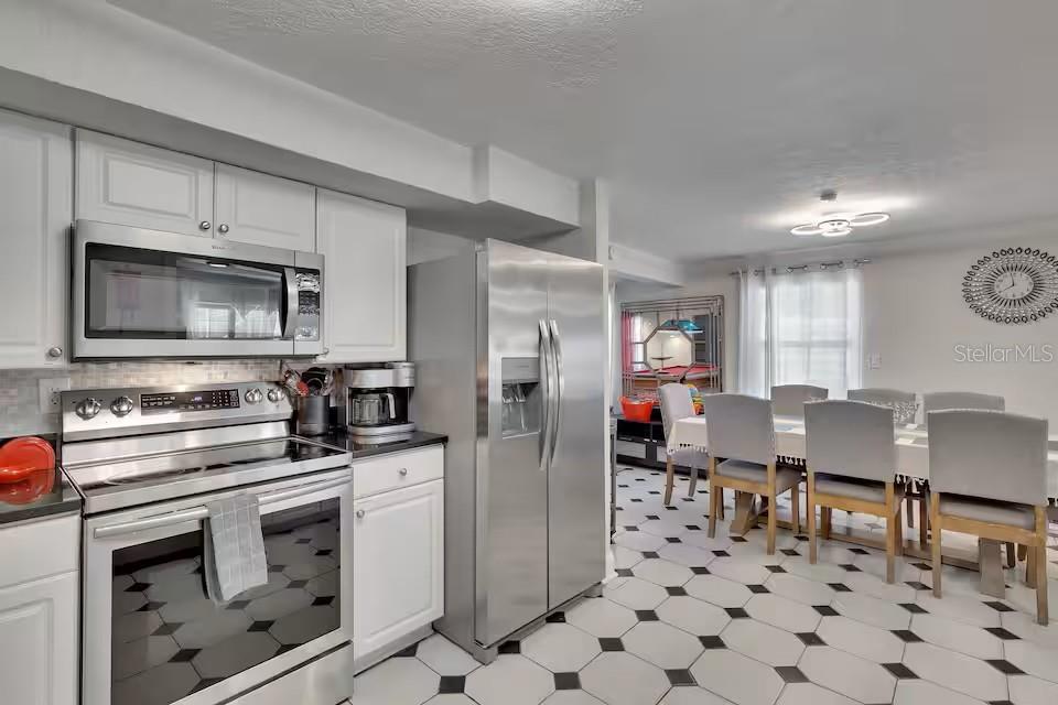 A kitchen with stainless steel appliances and white cabinets opens into a dining area — 10712 DALTON AVENUE, TAMPA, FL