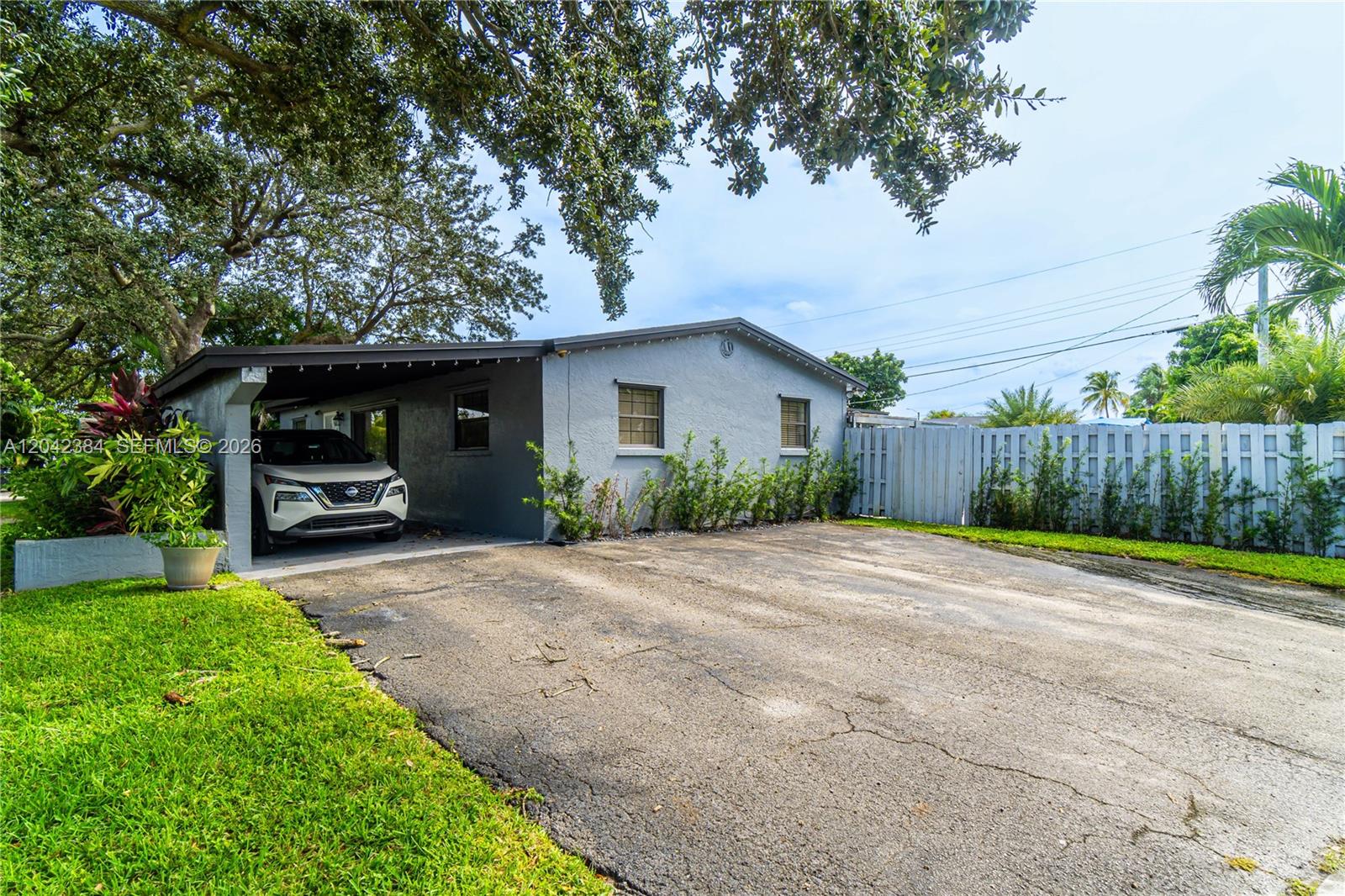 A gray single-story house features a carport, a paved driveway, and a white fence — 3338 Taft St, Hollywood FL 33021, HOLLYWOOD, FL