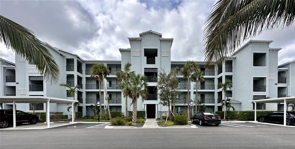 A multi-story apartment building with covered parking and palm trees under a cloudy sky — 14091 HERITAGE LANDING BOULEVARD UNIT 127, PUNTA GORDA, FL