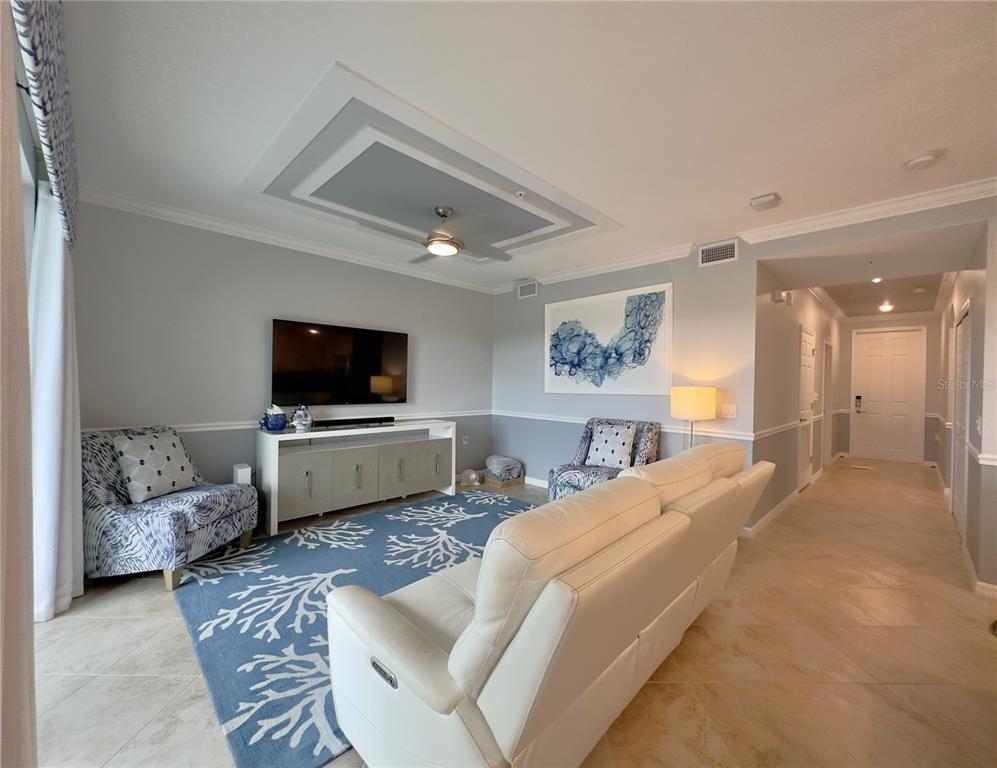 A living room features a white sofa, patterned armchairs, a blue coral-print rug, and television — 14091 HERITAGE LANDING BOULEVARD UNIT 127, PUNTA GORDA, FL
