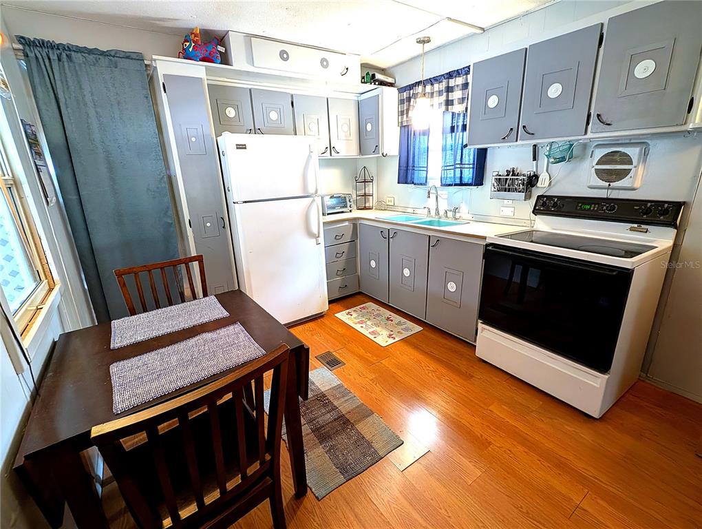 A kitchen features gray cabinets, white appliances, a wooden dining table, and hardwood flooring — 7803 46TH AVENUE N UNIT 49, ST PETERSBURG, FL