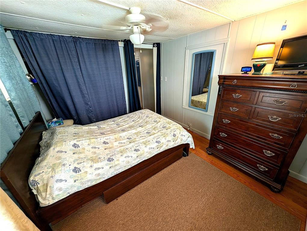 A bedroom features a wooden bed, a large dresser, a ceiling fan, and blue curtains — 7803 46TH AVENUE N UNIT 49, ST PETERSBURG, FL