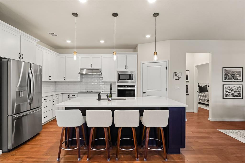 A modern kitchen features white cabinets, a dark blue island with bar seating, and stainless appliances — 17446 SAW PALMETTO AVENUE, CLERMONT, FL