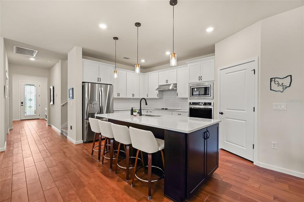 A modern kitchen features a dark wood island, white cabinetry, stainless steel appliances, and wood flooring — 17446 SAW PALMETTO AVENUE, CLERMONT, FL