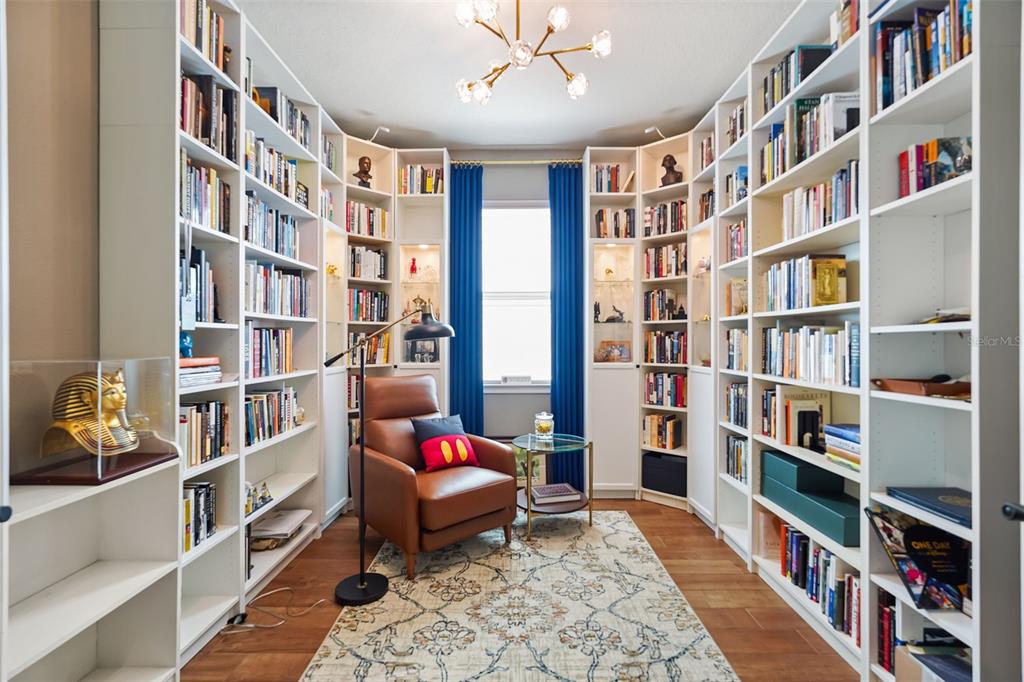 A home library features floor-to-ceiling white bookshelves, a leather armchair, and a central window — 17446 SAW PALMETTO AVENUE, CLERMONT, FL