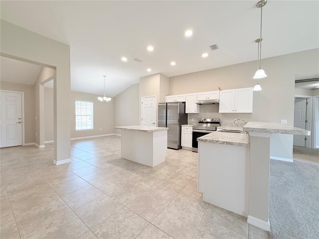 A kitchen with white cabinets, stainless steel appliances, and an island opens to a dining area — 15712 SW 37TH CIRCLE, OCALA, FL