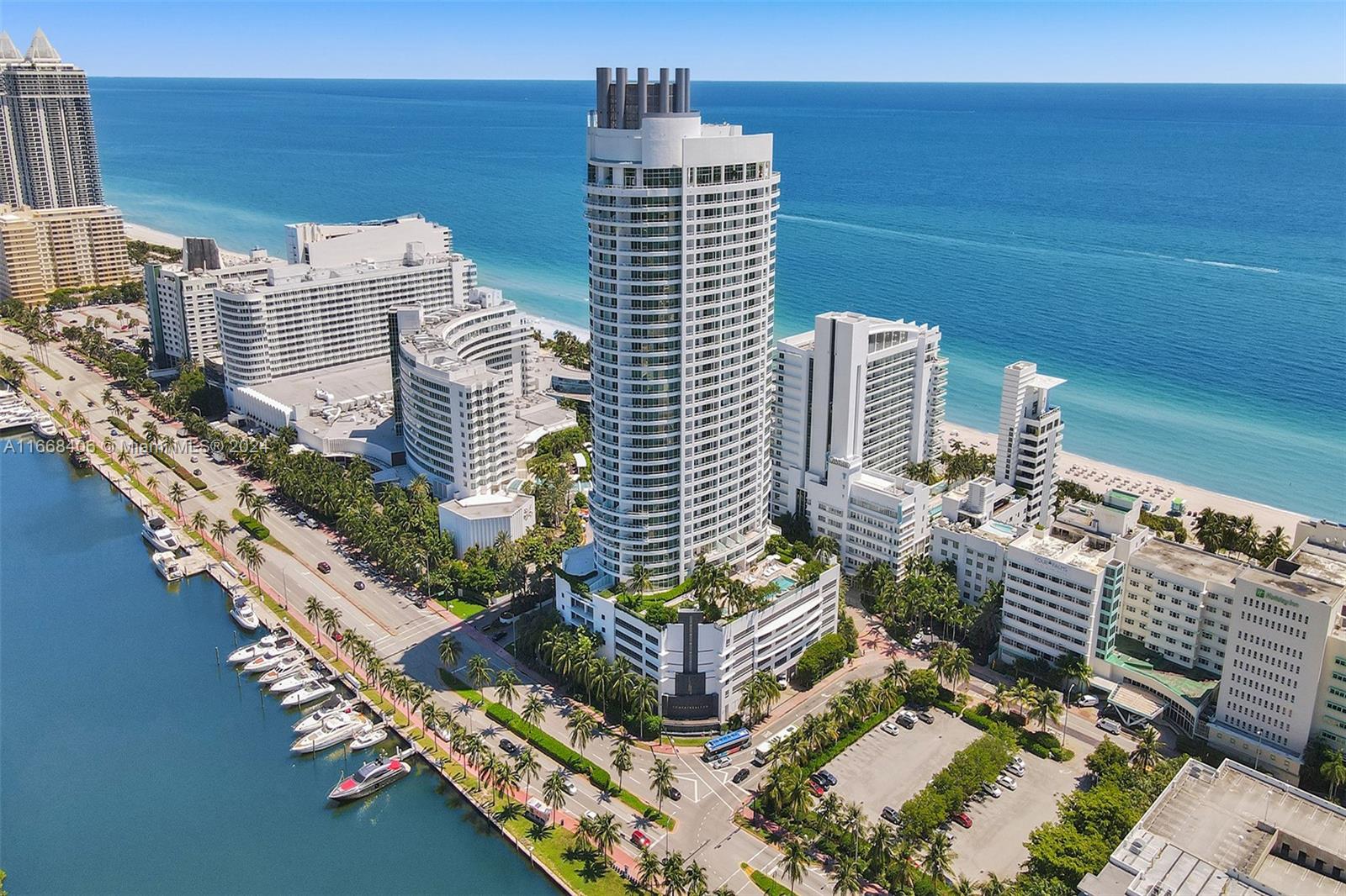An aerial view shows a tall cylindrical skyscraper surrounded by coastal buildings and a marina — 4391 Collins Ave, Miami Beach FL 33140, MIAMI BEACH, FL