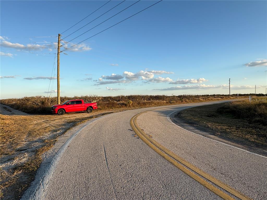 A red pickup truck is parked on the shoulder of a curved asphalt road — 627 RAULERSON ROAD, FROSTPROOF, FL