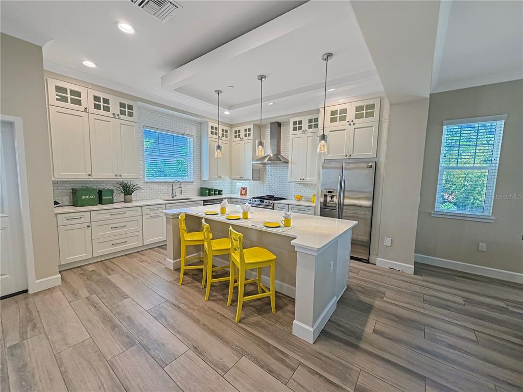 A kitchen features white cabinets, a central island with yellow stools, and wood-look tile flooring — 461 GERANIUM PARK WAY, WINTER GARDEN, FL
