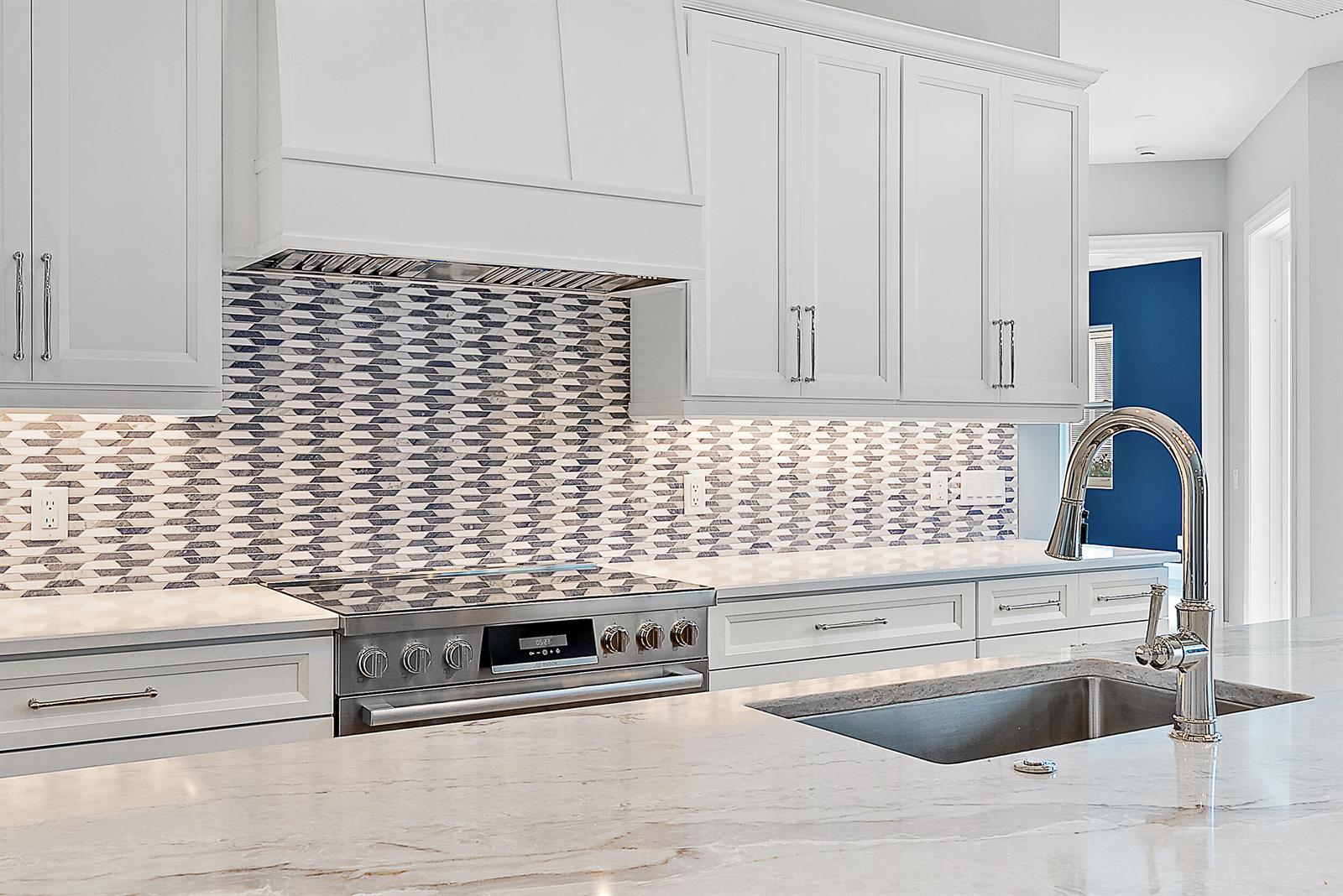 A kitchen features white cabinetry, a patterned tile backsplash, a stainless stove, and marble countertops — 248 Honeysuckle Drive, Jupiter FL 33458, JUPITER, FL